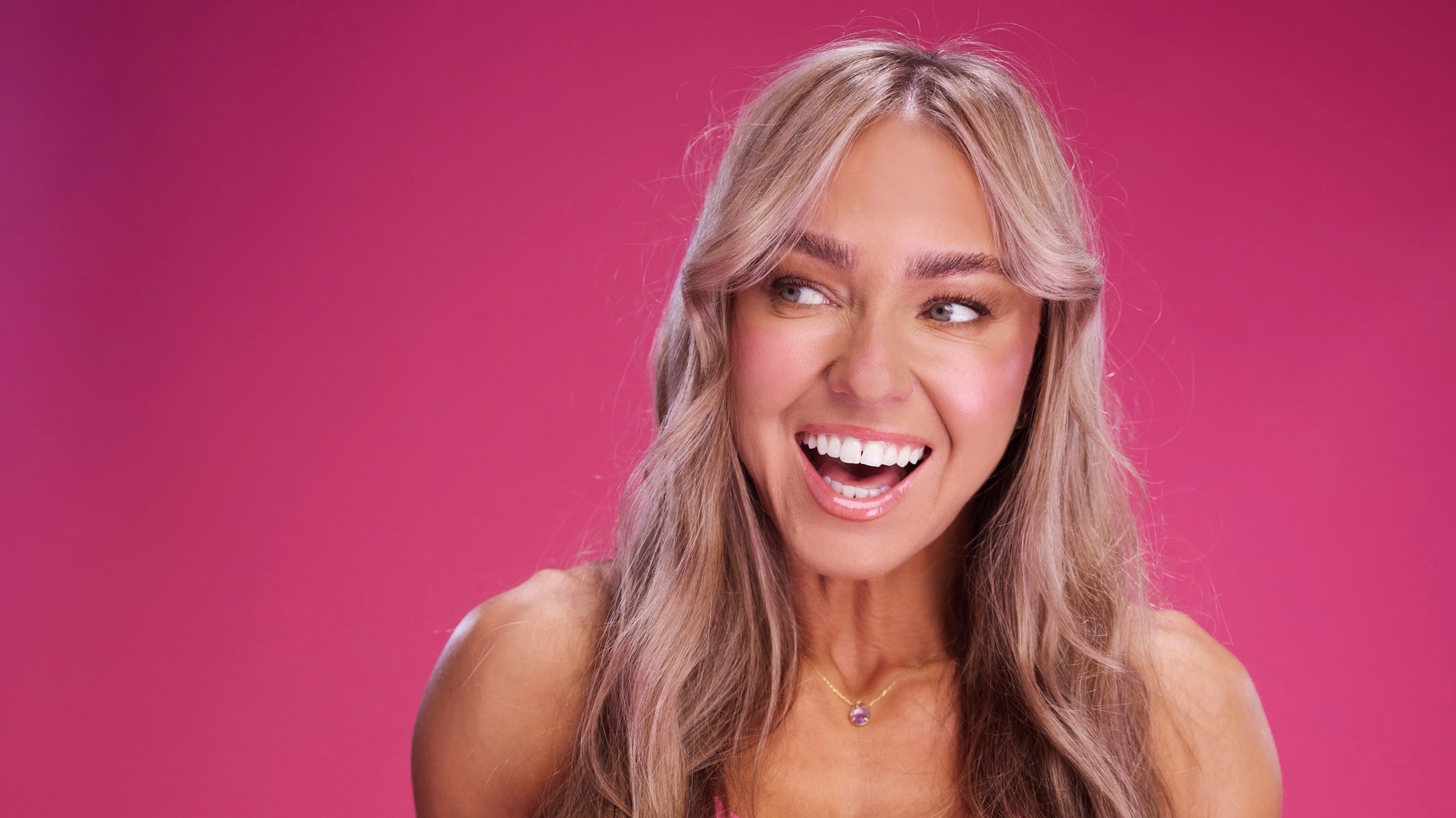 Caroline Girvan mid-laugh, glancing aside, pink on pink — the FUEL Program's 2026 register.